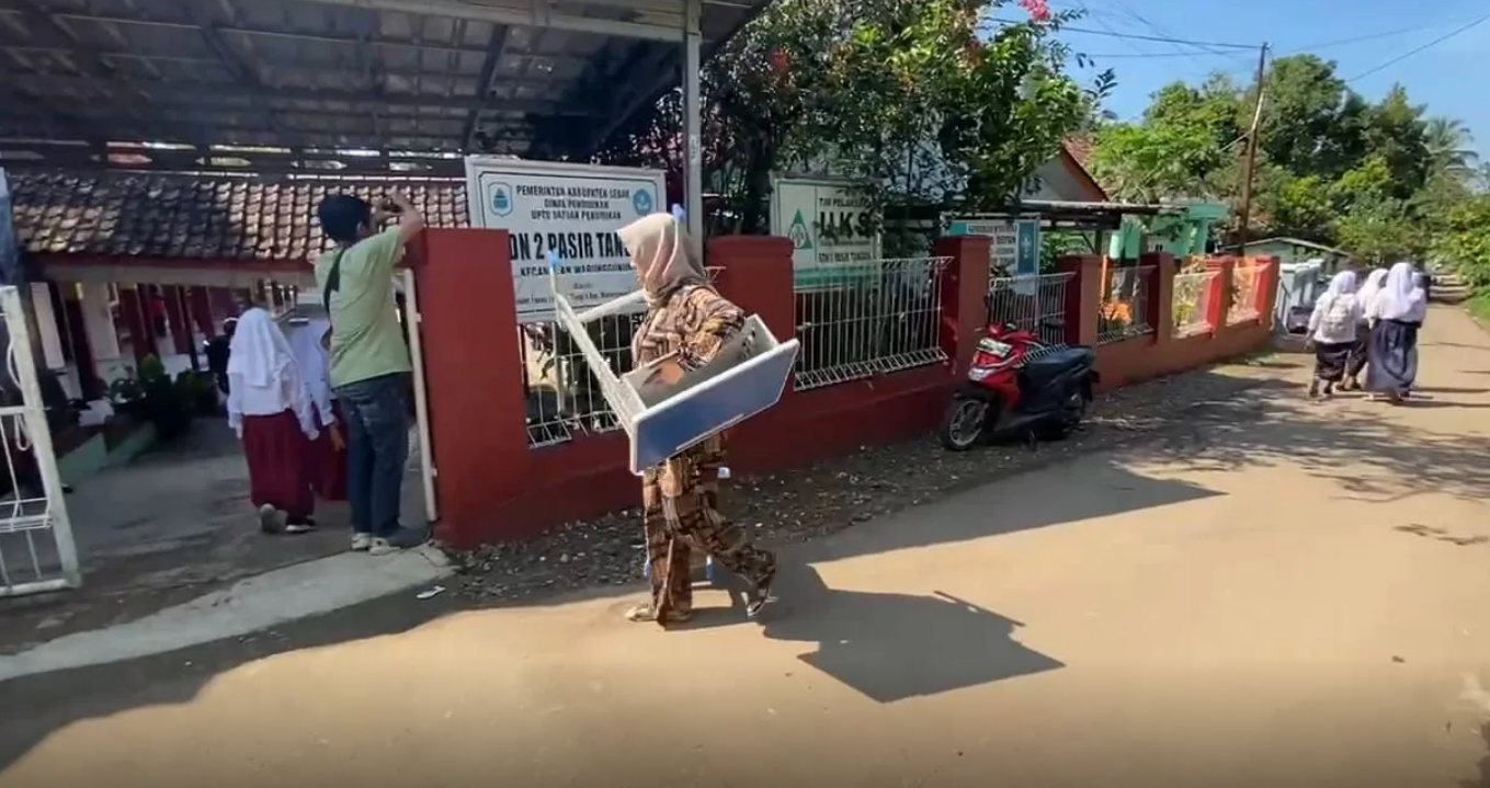 Arta Grace Monica, seorang ibu dari nurid SD 2 Pasir Tangkil gotong sendiri meja dan kursi pengganti ke sekolah.
