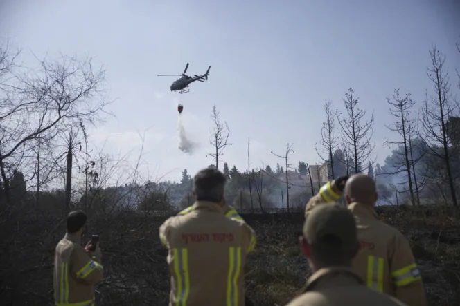 
					Sejumlah petugas pemadam kebakaran israel menyaksikan helikopter menyiram air di area kebakaran.