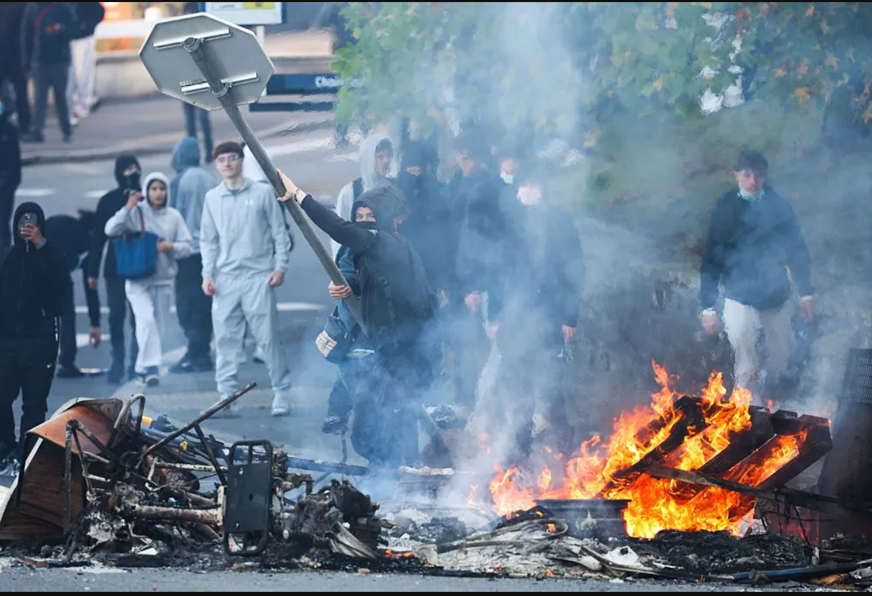 Seorang pendemo tampak akan melemparkan rambu lau lintas ke kobaran api dalam demo pelajar di Perancis. Jumat, 2 Oktober 2026. (REUTERS)