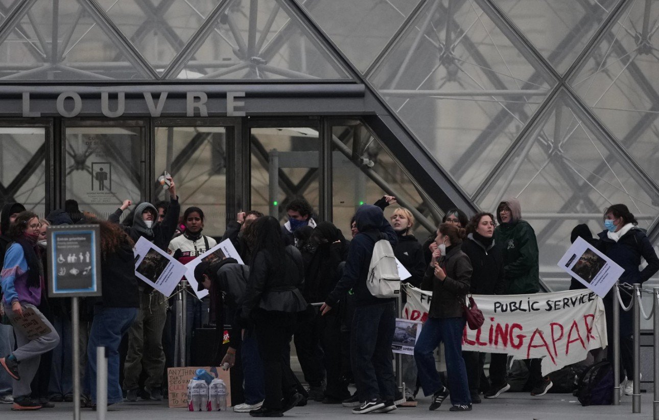 Para pekerja memblokir pintu masuk museum Louvre saat aksi protes menentang kenaikan biaya hidup di Paris, Senin, 19 Okt 2026. (AP Photo/Christophe Ena)