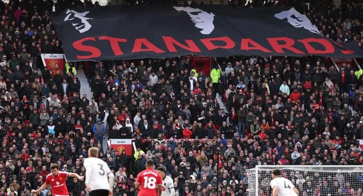 Sebuah spanduk bertuliskan “Standards” terbentang di tribun Stretford End. (Foto: BBC)